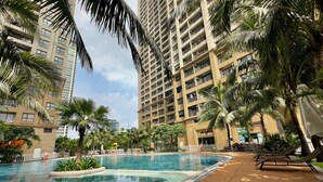 Una piscina con bordo in legno, circondata da palme e un edificio alto.