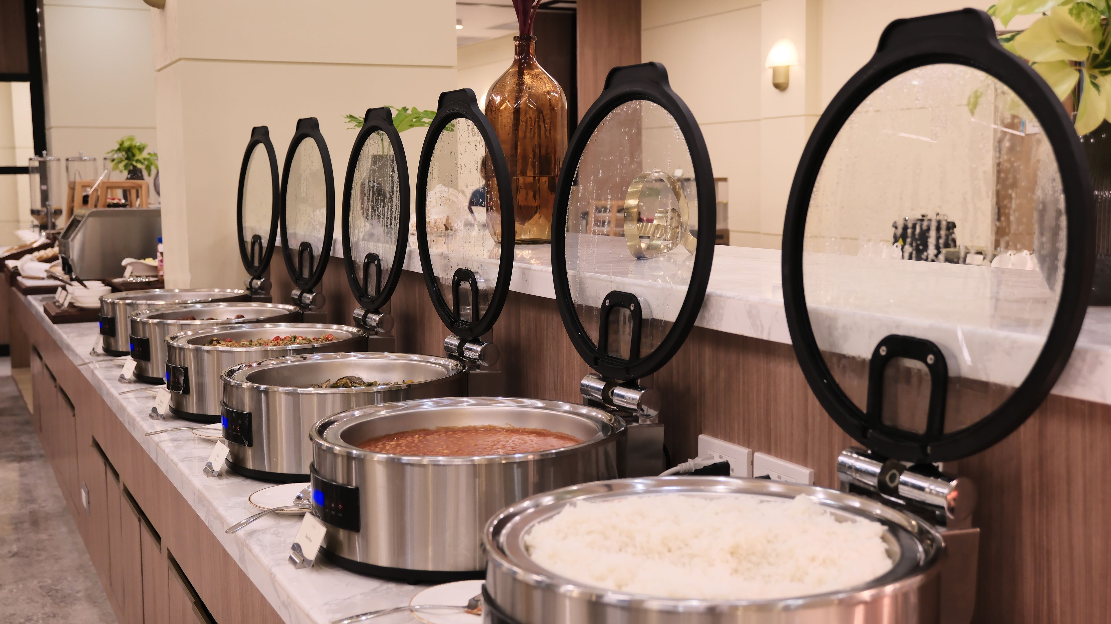 A buffet line with various food containers and a mirror.