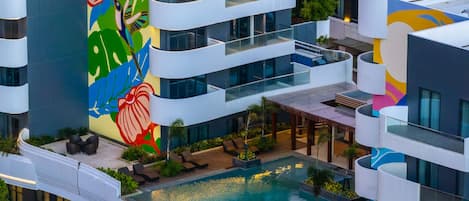Un hotel moderno con piscina en la azotea, asientos exteriores y un mural colorido.