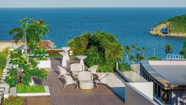Terraza en la azotea con mobiliario exterior, vista al mar y un promontorio rocoso.
