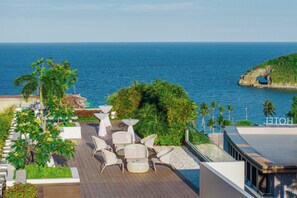 Terraza en la azotea con mobiliario exterior, vista al mar y un promontorio rocoso.