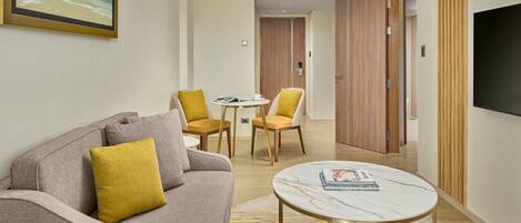 A modern hotel room with a sofa, two chairs, a small table, and a TV.