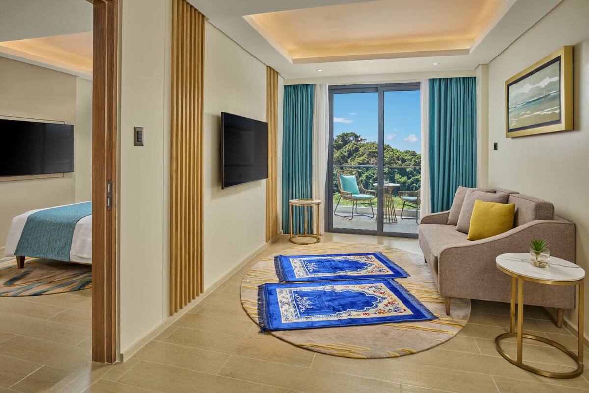 A modern hotel room with a bed, a sofa, a small table, and a TV.