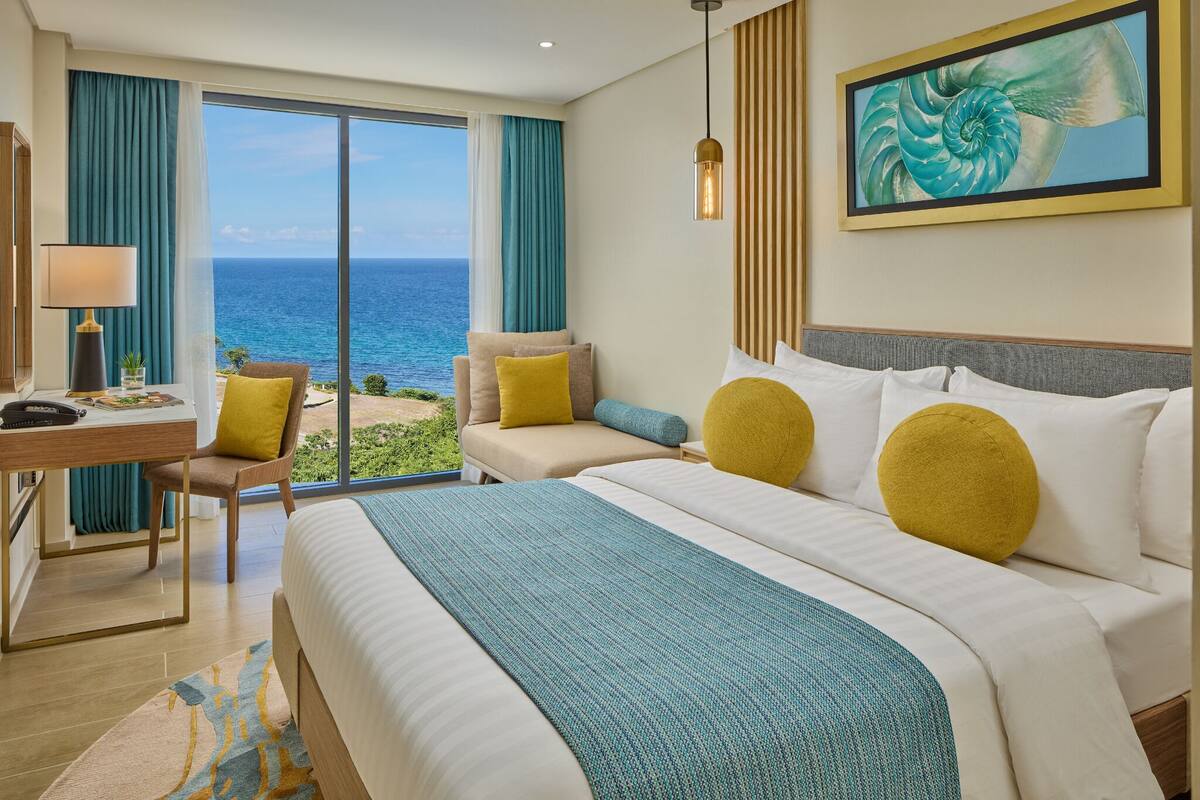 A hotel room with a large bed, a desk, and a view of the ocean.