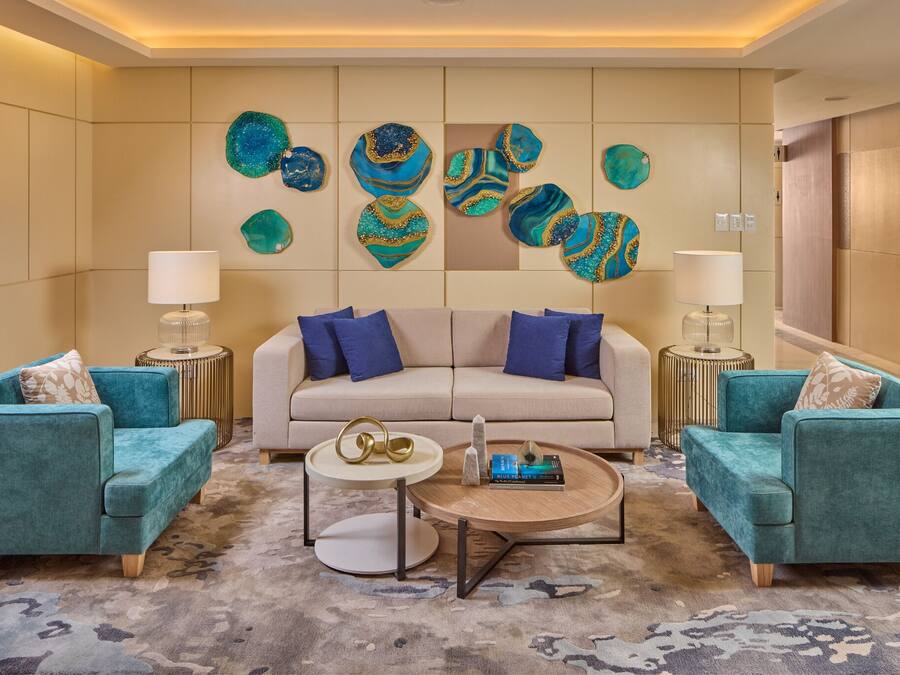 Ein modernes Wohnzimmer mit einem beigefarbenen Sofa, smaragdgrünen Sessel und abstrakter Wandkunst.