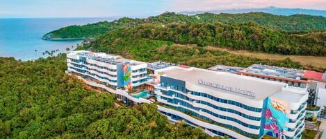 A modern hotel with multiple floors, a swimming pool, and a view of the ocean.
