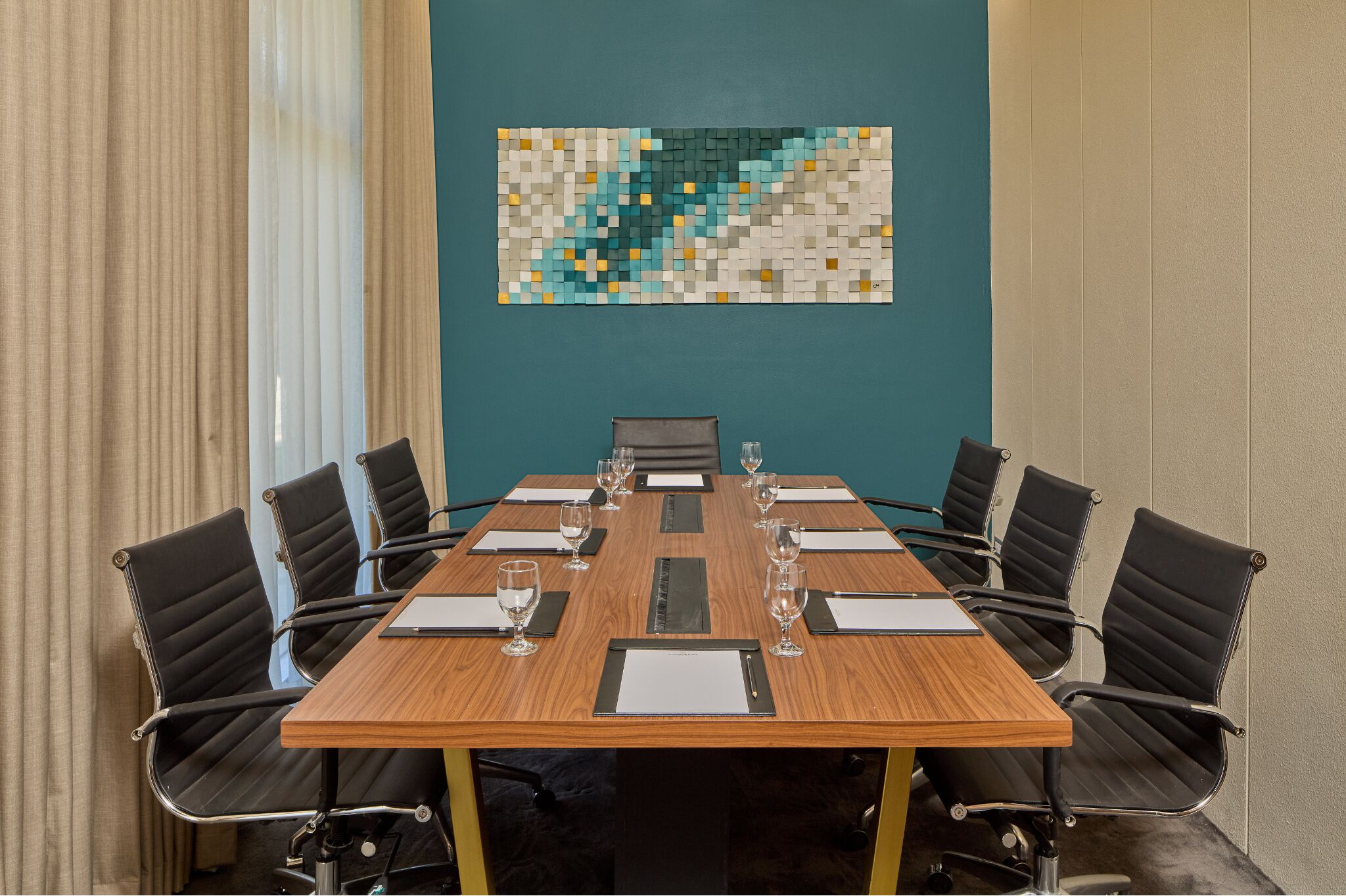 Une salle de conférence avec une table en bois, des chaises noires et un mur de couleur turquoise orné d’une œuvre d’art en mosaïque.