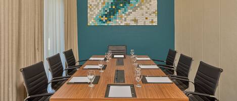 Une salle de conférence avec une table en bois, des chaises noires et un mur de couleur turquoise orné d’une œuvre d’art en mosaïque.