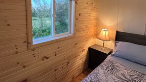 Una habitación con paneles de madera, una cama, una mesita de noche, una ventana y una lámpara.