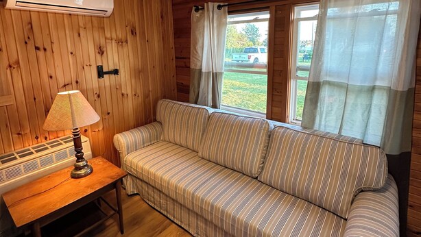 Una habitación con paneles de madera, un sofá a rayas, una mesa con lámpara y una ventana con cortinas.