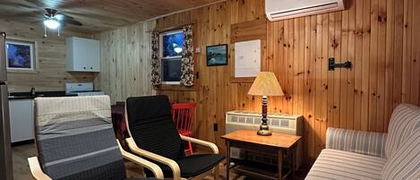 Et hyggeligt værelse med trævægge og -loft, seng, sofa, bord med lampe, stol og fjernsyn.