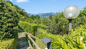 A pathway through a lush garden with a metal lamp post and a stone bench.