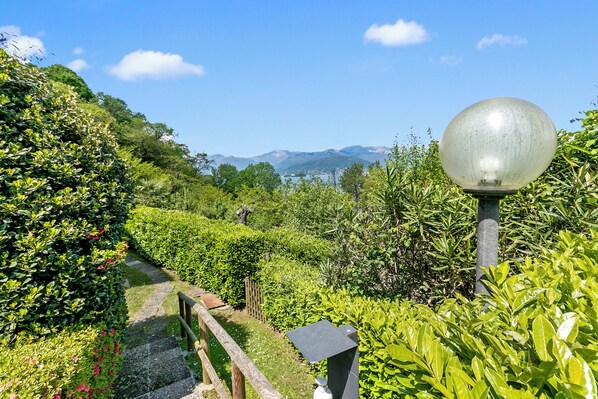 A pathway through a lush garden with a metal lamp post and a stone bench.