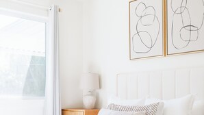 Une chambre moderne avec un grand lit, une table de chevet, une lampe et des œuvres d’art abstraites accrochées au mur.