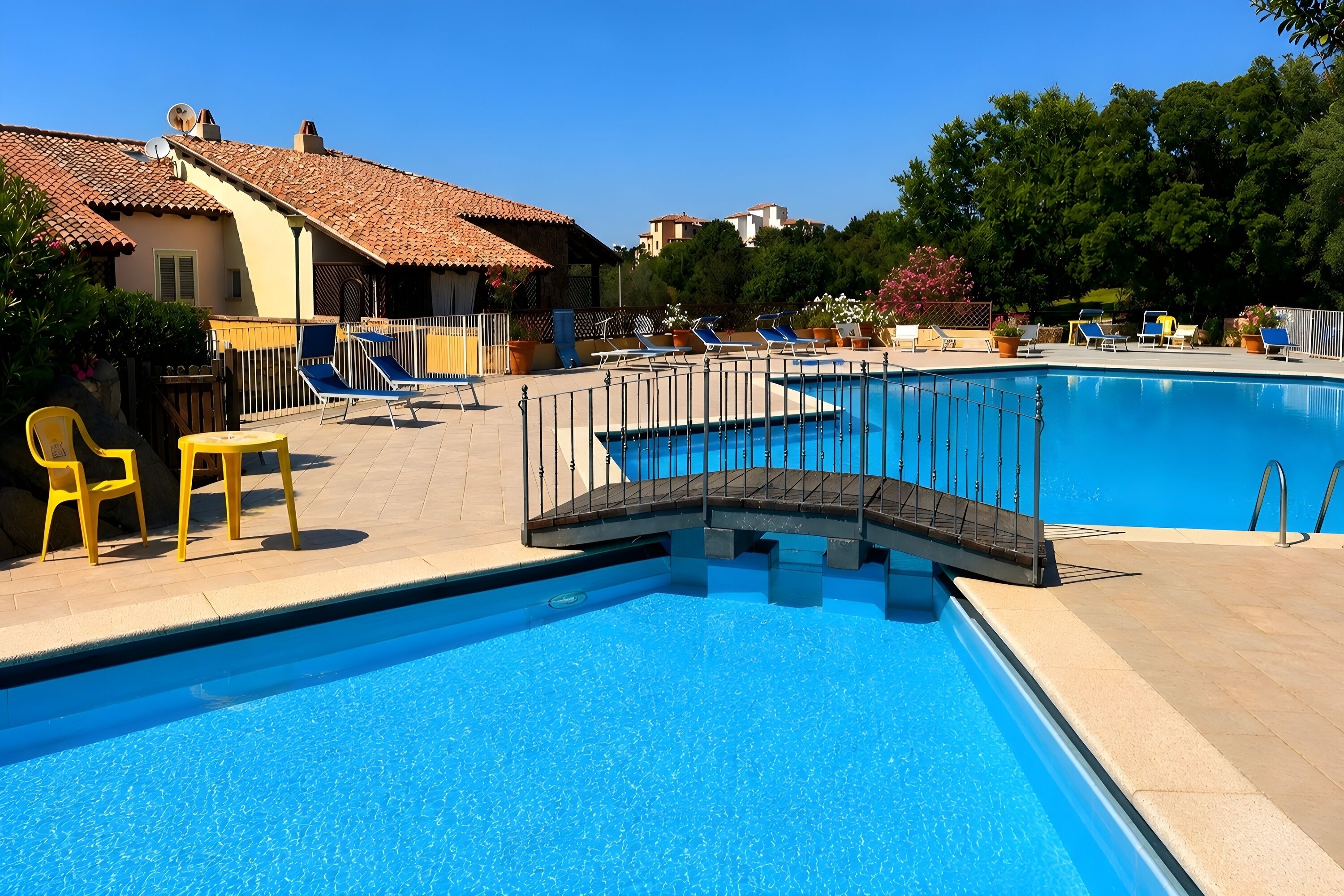 Una piscina amb un pont, gandules i un edifici amb teulada emblenquinada.