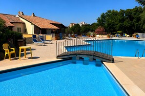 A swimming pool with a bridge, lounge chairs, and a building with a tiled roof.