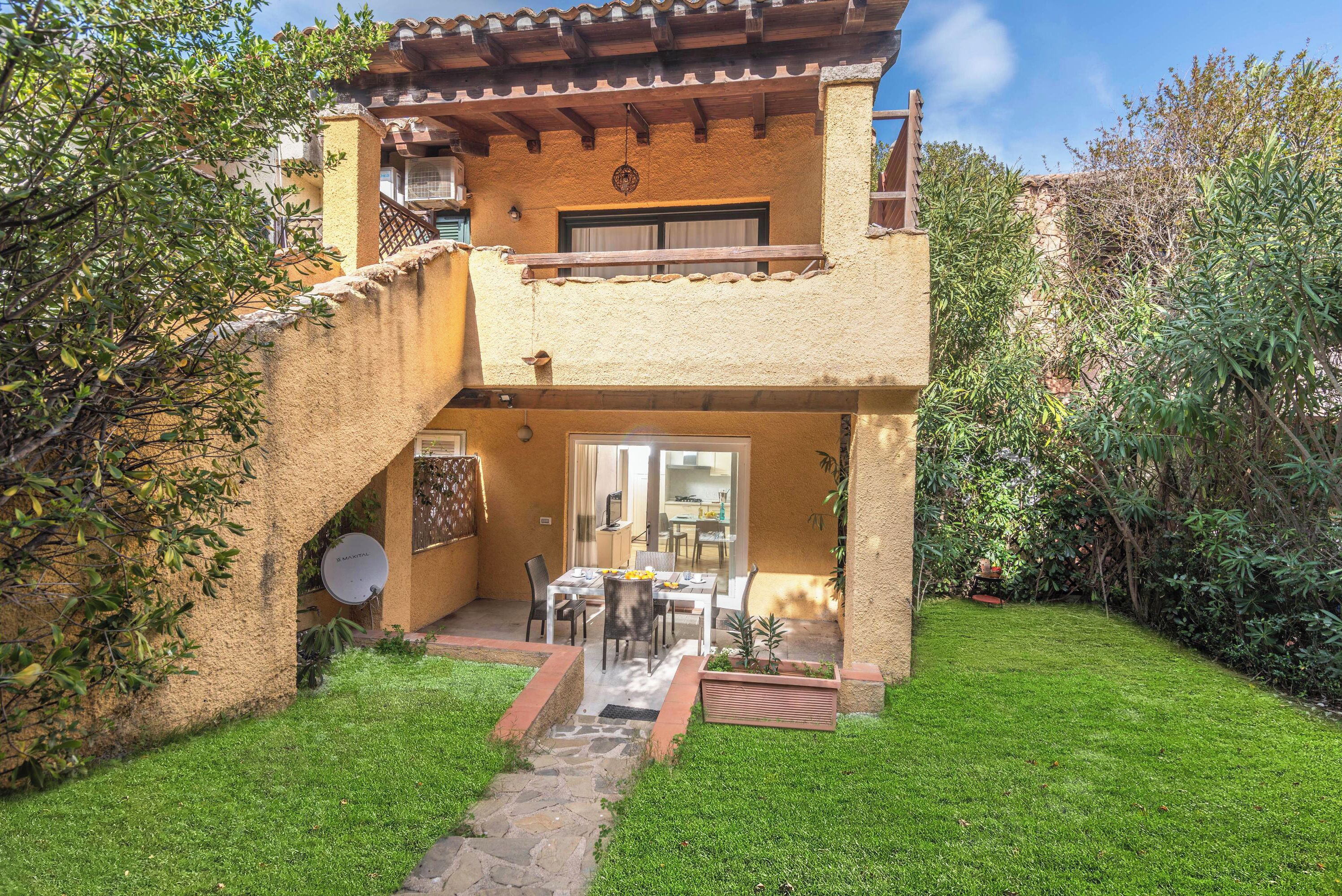 A two-story house with a balcony, a stone staircase leading to the entrance, and a well-maintained garden.