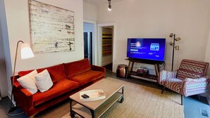 A modern living room with a red sofa, a coffee table, a television, and a patterned armchair. - Historic Downtown Raleigh 3-bedroom Home Close to Everything (Raleigh)