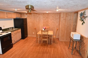 A compact kitchen with wooden walls, a dining table with chairs, a ceiling fan, and a microwave on a small table. - Bear Den | Full Kitchen Cabin Near Laurel River Lake & Cumberland Falls (Corbin)