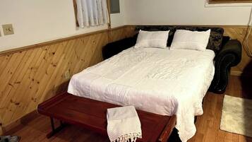 A wooden-paneled room with a bed, a bench, and a window with curtains.