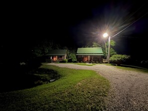 A cabin with a gravel driveway and a green lawn, illuminated by a single streetlight. - Bear Den - Cozy Lower Level Cabin · Laurel Lake ·Full Kitchen (Corbin)