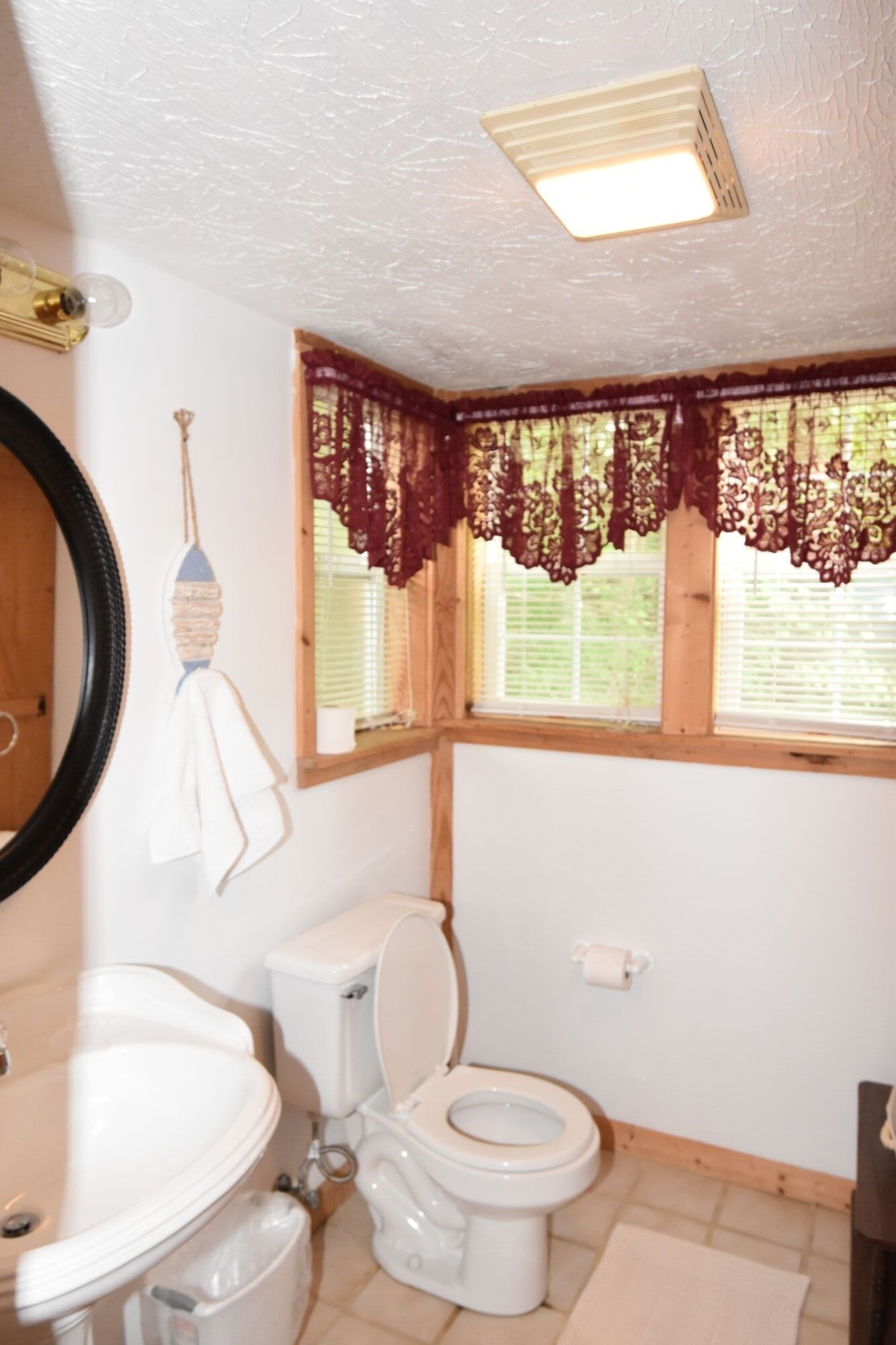Ein Badezimmer mit Toilette, Waschbecken und Fenster mit Spitzenvorhängen.