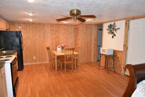 A kitchen with wooden walls, a dining table with chairs, a ceiling fan, and a microwave on a small table. - Bear Den | Full Kitchen Cabin Near Laurel River Lake & Cumberland Falls (Corbin)