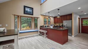 A spacious kitchen with a large island, wooden cabinets, and a view of the outdoors through large windows.