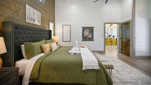 A bedroom with a tufted headboard, a large bed with green bedding, a bedside table with a lamp, and a ceiling fan.