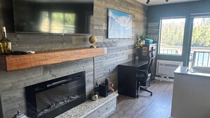 A modern living room with a flat-screen TV, fireplace, and a large window offering a view of the outdoors. - FLATHEAD LAKE WATERFRONT STUDIO RETREAT!!! WITH BOAT OPTION (Bigfork)