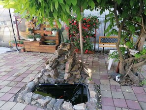 A garden with a pond, potted plants, and a wooden bench. - Pensiunea Ioana (Curtea De Arges)