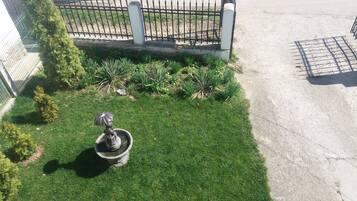 Een verzorgd gazon met een standbeeld van een persoon met een paraplu, omringd door diverse planten.