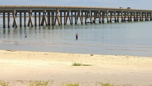En moler, der strækker sig ud i roligt vand, med en sandstrand i forgrunden.