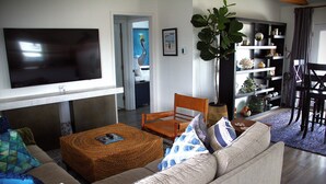 En stue med et fladskærms-tv, en sofa, et sofabord og en reol.