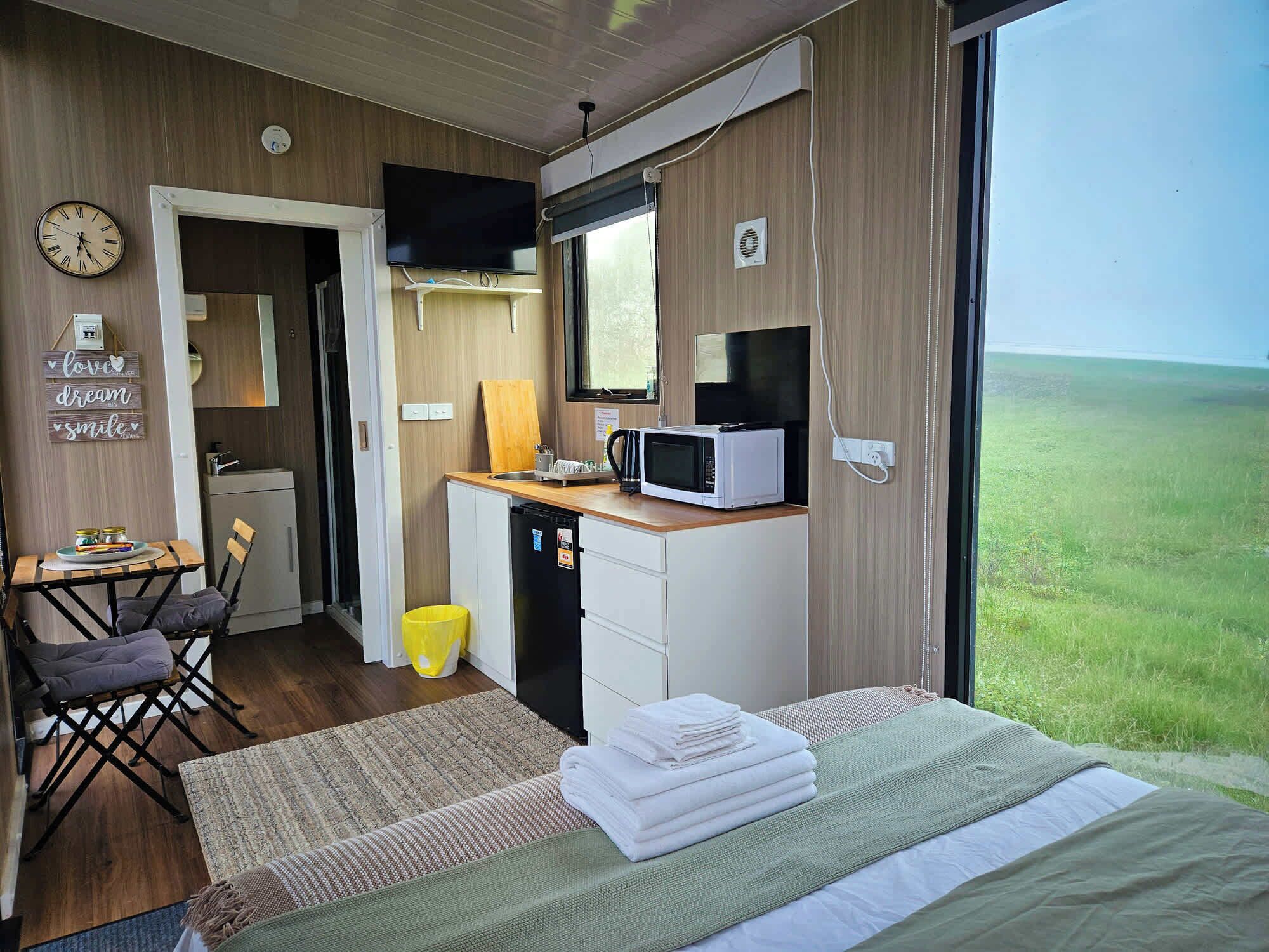 Ein gemütliches Schlafzimmer mit einem Bett, einem kleinen Schreibtisch mit einer Mikrowelle, einem Fernseher und Blick auf ein grünes Feld.
