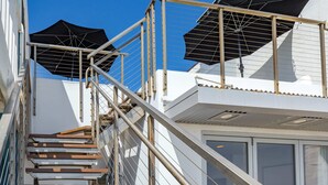 Eine Treppe führt zu einem Balkon mit Sonnenschirmen, einer Brüstung und Blick aufs Meer.