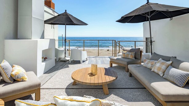 Eine Dachterrasse mit Meerblick, ausgestattet mit Sofas, einem Couchtisch und Sonnenschirmen.