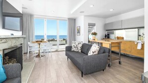 Ein modernes Wohnzimmer mit grauem Sofa, Kamin, Essbereich und Küche mit Meerblick.