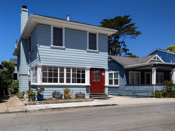 A two-story house with a red door, multiple windows, and a porch.