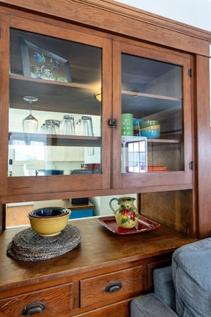 A wooden cabinet with glass doors, a woven placemat, and a ceramic pitcher. - Capitola Village Craftsman Cottage- 4 min to beach (Capitola)
