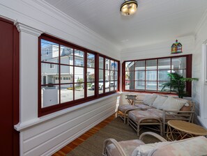 A sunroom with large windows, wicker furniture, and a small table.