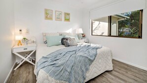 Un dormitorio con cama, mesitas de noche, ventilador de techo y un amplio ventanal con vistas a zonas verdes.