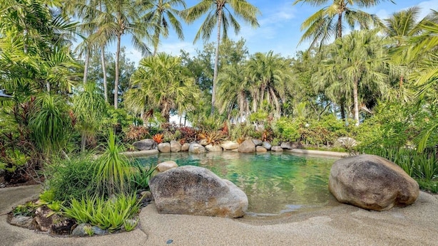 Piscina de un resort tropical rodeada de palmeras y rocas.