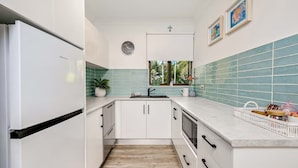 Una cocina moderna con armarios blancos, un refrigerador de acero inoxidable, una ventana con vista a vegetación y un salpicadero de azulejos.