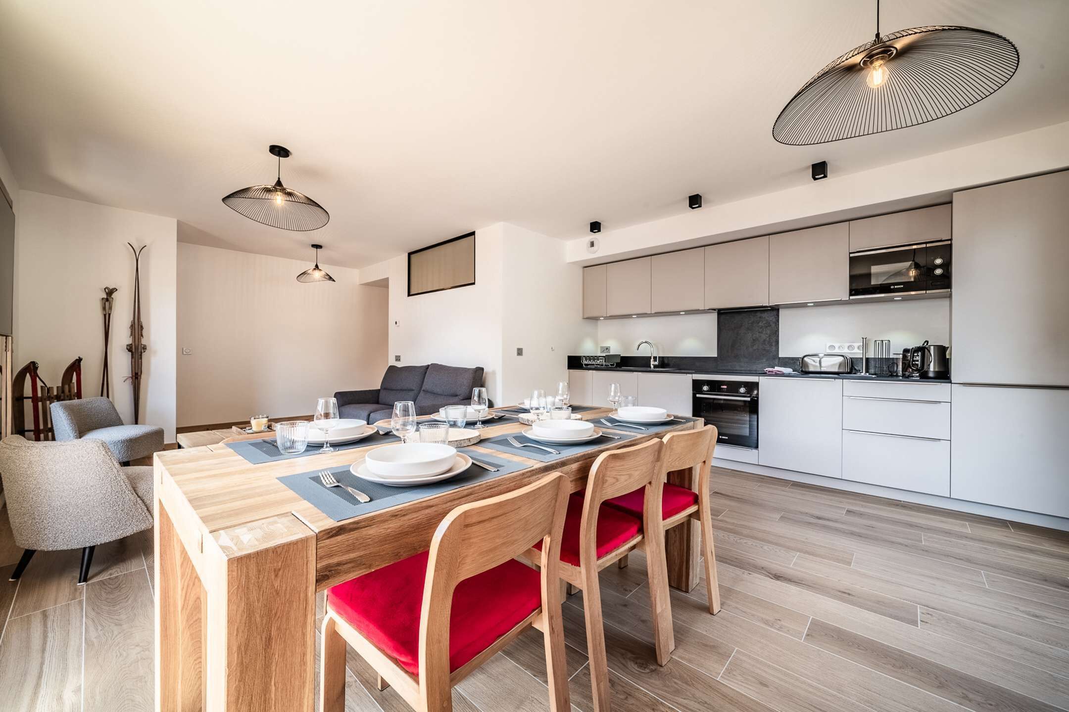 A modern kitchen with white cabinets, a built-in oven, and a dining area with a wooden table and red chairs.