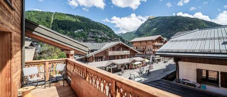 A wooden balcony with a view of a mountainous village, wooden buildings, and a clear sky.