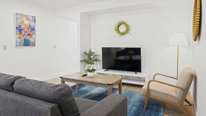 Una sala de estar con sofá, una mesa de centro, televisor y una planta.