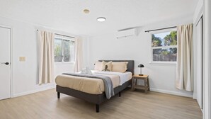 Un dormitorio con cama, mesita de noche, ventana y aire acondicionado.