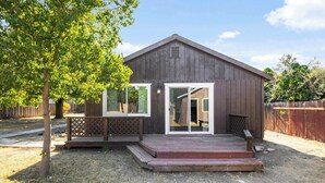 Una pequeña construcción de madera con porche, puerta corrediza de vidrio y patio cercado.