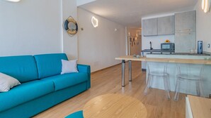 A modern living room with a teal sofa, a wooden coffee table, and a kitchen area with a microwave and bar stools. - Sea view apartment in Porto Azzurro (Porto Azzurro)